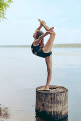 teenage girl in a swimsuit and barefoot does exercises from rhythmic gymnastics in nature on the...