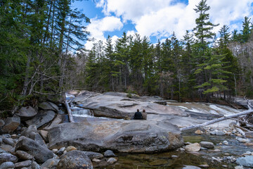 Two tourists - a man and a woman sit on huge flat stones on a Waterfall on the Pemigewasset River (The Pemi). Lincoln Woods Trail. White Mountains National Forest, NH