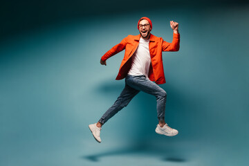 Fototapeta na wymiar Happy man dressed in jeans and orange jacket runs on blue background