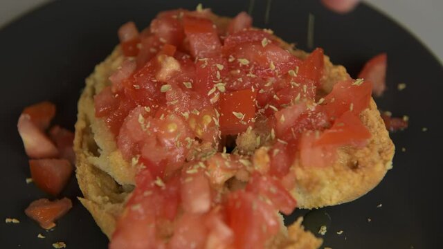 A man prepare a friselle, typical dish of Puglia: dry bread with tomatoes, oregano and olive oil: sprinkle oregano on the frisa. Healthy vegetarian vegan food