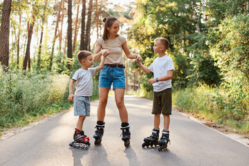 Outdoor shot of happy family having fun and roller skating together in summer park, mommy holding...