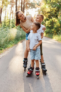 Happy Smiling Woman Roller Skating With Her Children In Summer Park, Mother Looking At Kids With Toothy Smile, Family Rollerblading And Having Fun Together.