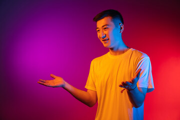 Portrait of Asian young man isolated on studio background in gradient pink purple neon light,...