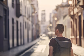 Rear view of solo traveler. Young man with backpack on street of old town. San Cristóbal de La...