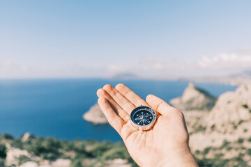 Compass in male hands in the background sea and mountains.