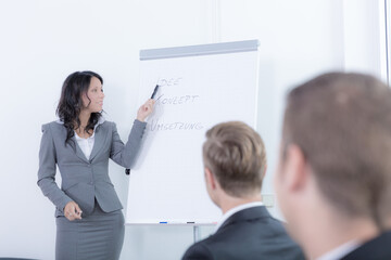 Young business woman wearing a blazer is working at a flip chart in front of a group of listeners