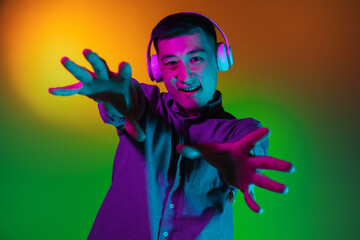 Portrait of Asian young man isolated on studio background in gradient green yellow neon light, colour filter. Concept of human emotions, facial expression.