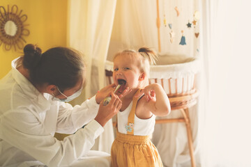 funny little girl Toddler shows her throat to nurse in mask and white coat, calling doctor at home, patronage. Examination of pediatrician in a real interior,concept of medicine and disease prevention