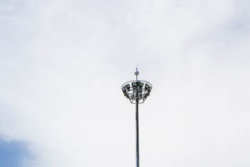 Remote photo of big spotlight pole. with fluffy white cloud with bright sunlight background. Beautifully shaped set in a park to illuminate the night. technology that gives light for safety at night.