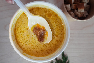 Close-up of mushroom soup in a paper glass. Takeaway food in the restaurant. The concept of vegetarian fast food in the meal industry. Pieces of crackers float in the broth.