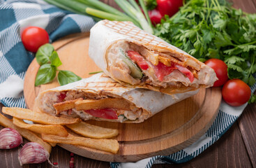 Shawarma with chicken, vegetables and French fries on a wooden table.