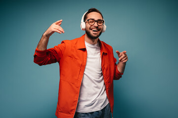 Positive man in orange jacket smiles and enjoys music in headphones