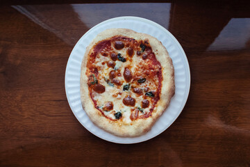 A close-up of a mini pizza in a disposable dish. Top view of takeaway food in fast food cafe. The photo shows mozzarella cheese, tomatoes, olives and various sausages. Meal for one person