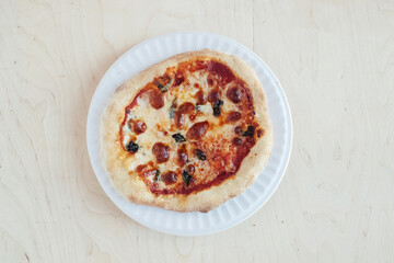 A close-up of a mini pizza in a disposable dish. Top view of takeaway food in fast food cafe. The photo shows mozzarella cheese, tomatoes, olives and various sausages. Meal for one person