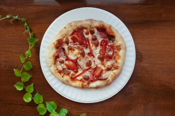 A close-up of a mini pizza in a disposable dish. Top view of takeaway food in fast food cafe. The photo shows mozzarella cheese, tomatoes, olives and various sausages. Meal for one person