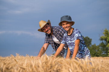 Naklejka na ściany i meble Happy father and son are standing in their grown wheat field before harvest.