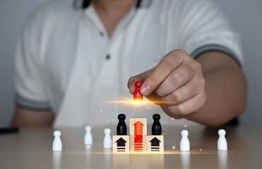 
Organizational Leadership Selection Concept, Outstanding Management Ability, Leadership. A man's hand picks up a wooden doll and places it on a block with rising arrows. individual status