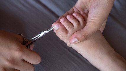 Obraz na płótnie Canvas Closeup of female hands holding scissors to cut toe nails on tiny baby foot. Mom taking care of her child s hygiene