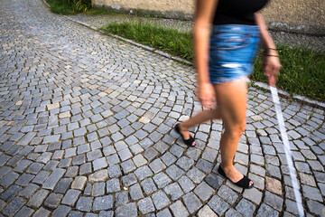 Blind woman walking on city streets, using her white cane to navigate the urban space better and to...