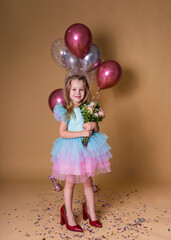 little girl stands in her mother's shoes and holds a bouquet of fresh flowers on a beige background with a place for text