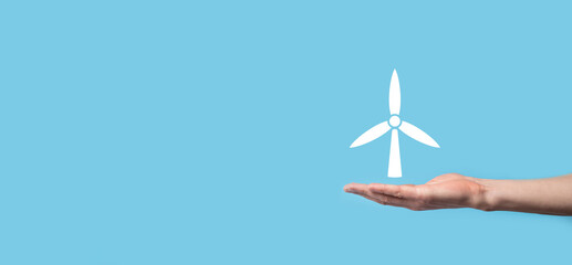 Hand holding an icon of a windmill that produces environmental energy on blue background.