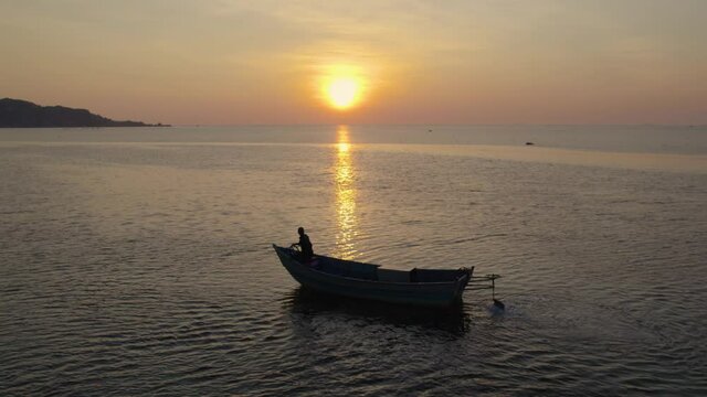 Aerial view of fisherman in his boat searching for fish during golden hour. Silhouette.