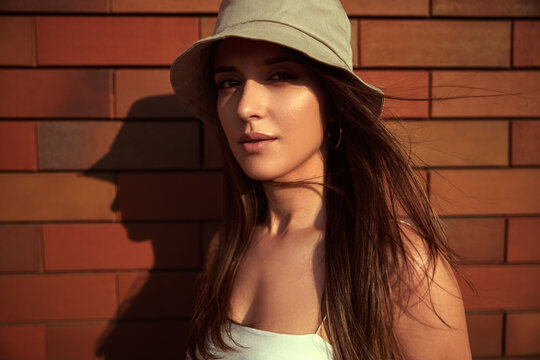 Young woman in hat standing near brick wall
