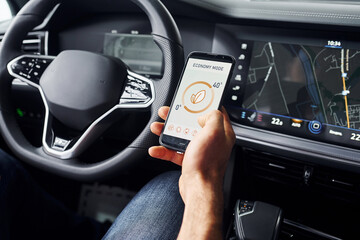 Sits in the car. Close up view of man's hand that holds phone with labels and icons. Conception of remote control