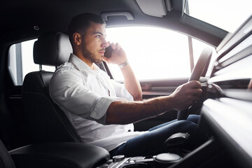 Young man in white shirt is sitting inside of a modern new automobile