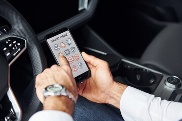 Sits in the car. Close up view of man's hand that holds phone with labels and icons. Conception of remote control