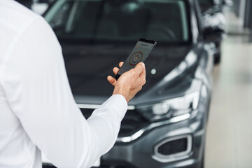 Black car. Close up view of man's hand that holds phone with labels and icons. Conception of remote control
