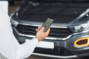 Black car. Close up view of man's hand that holds phone with labels and icons. Conception of remote control