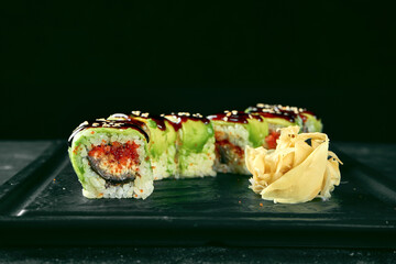 Sushi Roll green dragon with avocado, eel and tobiko caviar on a black plate on a dark background. Food delivery. Japanese cuisine