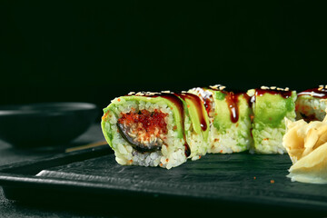 Sushi Roll green dragon with avocado, eel and tobiko caviar on a black plate on a dark background. Food delivery. Japanese cuisine