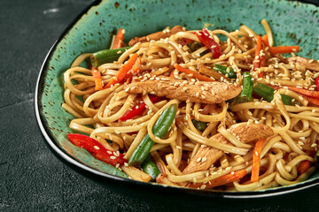 Buckwheat udon wok noodles with chicken, vegetables cilantro sauce in a green plate. Close up,...