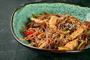 Buckwheat udon wok noodles with chickenl, vegetables, sauce in a green plate. Close up, selective focus