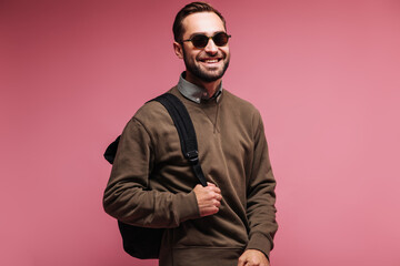 Obraz premium Handsome man in sunglasses and brown sweater holding backpack