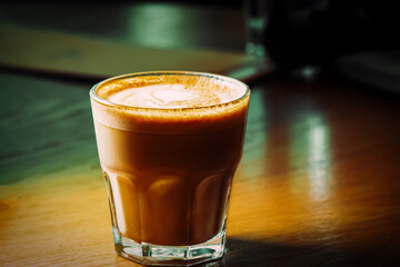 Flat-white coffee in small glass served on wooden tabletop.