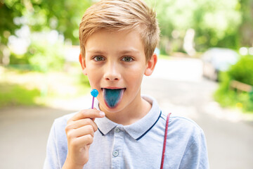 Teen blonde boy licking lollypops and showing colored blue tongue. Concept of food coloring in...