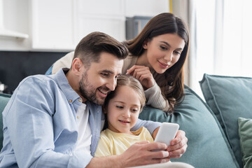 happy man using mobile phone near daughter and wife at home