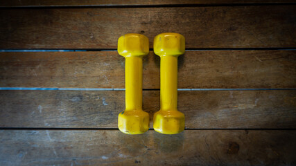Top view of pairs of 1 kilogram yellow mini dumbbells on wooden backgrounds. Exercise tool and...