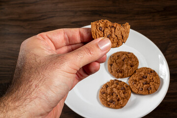 Male hand pick up a chocolate chip cookie from top view. Wooden Background, selective Focus