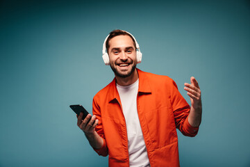 Active man in orange outfit posing in headphones and holding phone