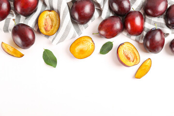 Close up image of juicy organic whole and halved plums with green leaves & visible core texture, isolated white background, copy space. Macro shot of fruit slices. Top view, flat lay.