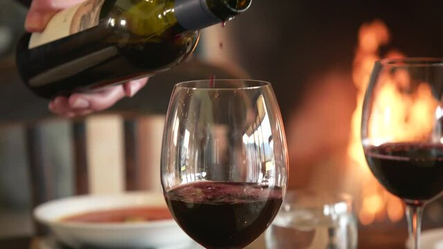 Red wine pouring into crystal glass on table with fireplace in background