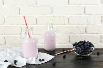 Two blueberry milkshake bottles on black wooden table. Couple of protein shake drinks with berries on kitchen counter. White brick wall background. Clean eating concept. Copy space, close up, top view