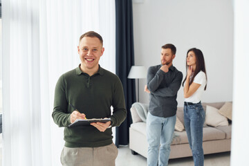 Salesman helps young couple in choosing an apartment. Conception of business and rent