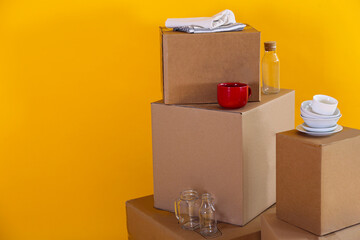Bunch of blank moving boxes with dishes and kitchen appliances in a new apartment. Room with freshly painted yellow walls, unpacked cardboard boxes. Interior background, copy space for text.