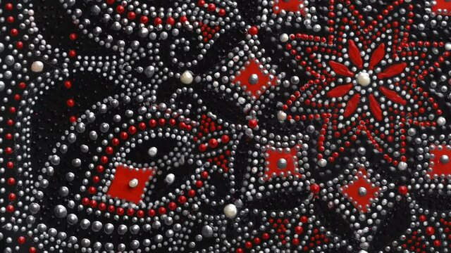 Decorative ceramic plate with red and silver colors, painted plate rotating on background, closeup, top view. Decorative porcelain plate painted with acrylic paints, handwork, dot painting
