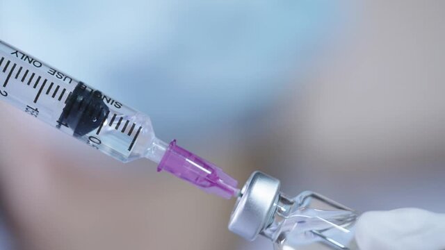 Closeup of nurse  using syringe sucks a coronavirus vaccine out of bottle, with her hands wear rubber gloves and face mask, modern medical health protection concepts, anesthetic hypodermic syringe, 